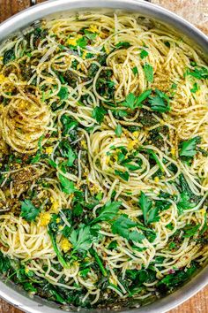 a pan filled with pasta and greens on top of a wooden table