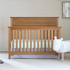 a white sheep standing next to a wooden crib in a room with gray carpet