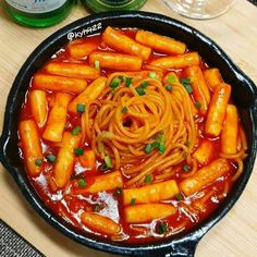 a skillet filled with spaghetti and carrots on top of a wooden cutting board