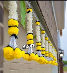 yellow and white flowers are hanging from the side of a building, along with black and white pom - poms