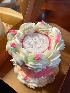 a decorated cake sitting in a box on top of a wooden table next to a cupcake