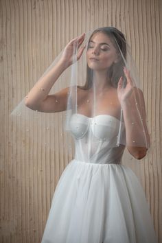 a woman wearing a white dress and veil with her hands on her head, standing in front of a wooden wall