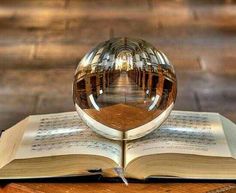 an open book sitting on top of a wooden table next to a glass ball in the middle