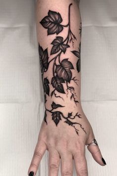 a woman's hand with black flowers and leaves tattoo on it, while she is holding