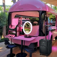 a pink bus is parked on the side of the road with its doors open and luggage in front of it