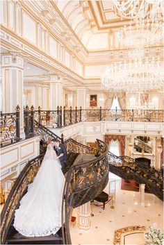 a bride and groom are standing on the stairs in an ornate building with chandeliers