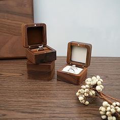 three wooden boxes with wedding rings in them sitting on a table next to some flowers