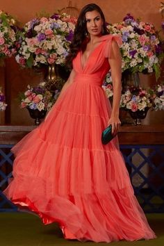 a woman in an orange dress standing next to flowers and holding a green clutch bag