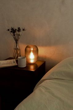 a lamp that is on top of a night stand next to a book and vase