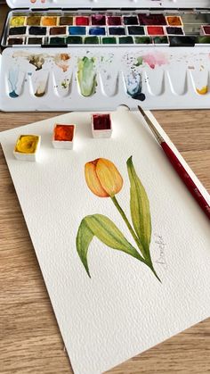 a watercolor painting of a tulip with paintbrushes on the table next to it