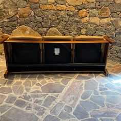 a wooden bench sitting on top of a stone floor next to a wall with two bins