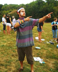 a man pointing at something while standing on top of a grass covered field with other people in the background