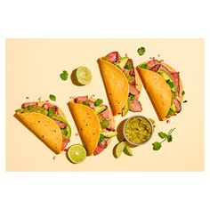 three tacos with guacamole and limes on the side next to it