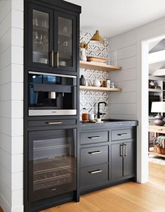 a kitchen with black cabinets and white walls, wood flooring and open shelving