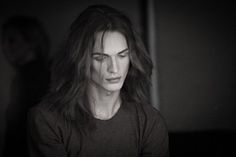 a woman with long hair looking at her cell phone while standing in a dark room