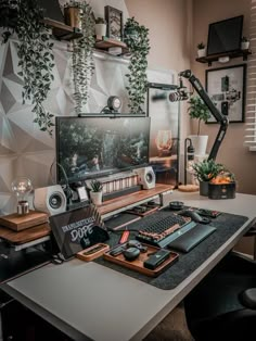 a desk with a monitor, keyboard and other items on it in front of a plant