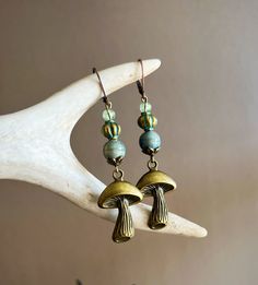 Earthy and whimsical, these handmade mushroom earrings are the perfect addition to any outfit Materials: Brass mushrooms, ceramic beads, metal beads, lever back ear hooks. Lead and nickel free. Drop length: 2in Whimsical Adjustable Mushroom Design Jewelry, Whimsical Green Mushroom Earrings, Cute Handmade Mushroom-shaped Earrings, Nature-inspired Dangle Earrings With Mushroom Design, Whimsical Mushroom-shaped Earrings For Gifts, Woodland Earrings, Mushroom Jewelry, Mushroom Fairy, Metal Stamped Jewelry