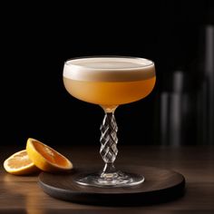 a glass filled with liquid next to an orange slice on a wooden plate and black background