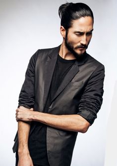 a man with his arms crossed wearing a black shirt and blazer, standing in front of a white background