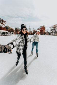 two girls skating on an ice rink in the winter with one holding her hand out