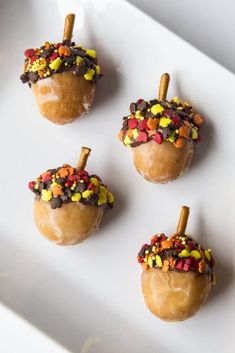 four caramel apples decorated with candy and sprinkles on a white plate