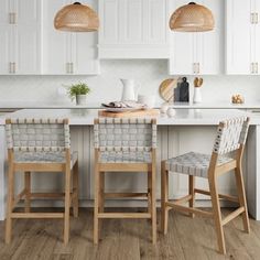 a kitchen with white cabinets and wooden chairs in front of an island countertop that has two pendant lights hanging above it