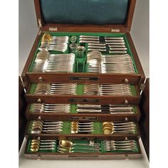 a set of silverware in a wooden box with green trimmings and handles