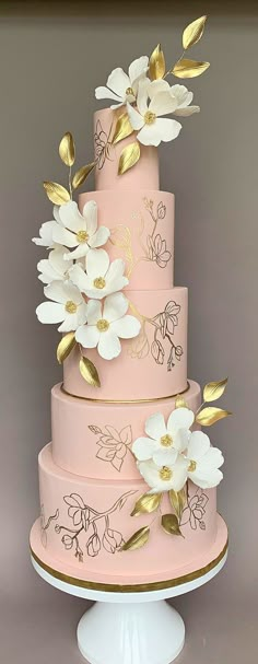 a pink and gold wedding cake with white flowers on the top tier is sitting on a pedestal