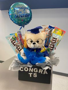 a graduation teddy bear sitting on top of a box filled with candy and candies