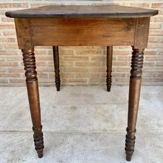 an old wooden table sitting in front of a brick wall with two legs on it