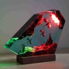 a green and red glass sculpture on top of a wooden stand with an orange light coming from it