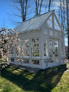 a small white house sitting on top of a green grass covered field next to trees