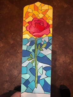 a hand holding up a stained glass piece with a red rose on it's side