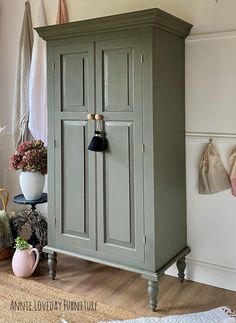 a green armoire sitting on top of a wooden floor next to a potted plant