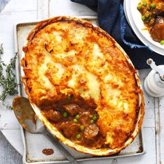 a casserole dish with meat and vegetables in it on a tray next to two plates