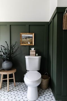 a white toilet sitting in a bathroom next to a wooden stool and potted plant