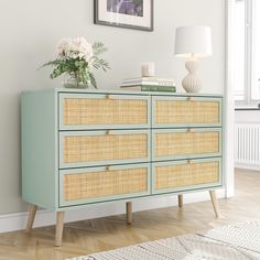 a blue dresser with wicker drawers and white flowers on top in a living room