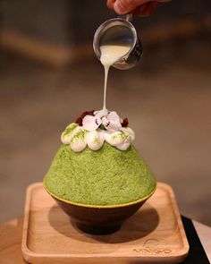 a person is pouring something into a green dessert on a wooden tray with white flowers