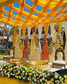 an outdoor wedding setup with yellow and white flowers on the ground, decorated in gold and orange