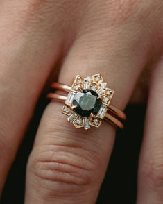 An art deco style engagement ring and matching tracer wedding band are shown on a woman's ring finger. This 14K rose gold wedding ring set features a round brilliant cut salt and pepper diamond center stone surrounded by a diamond halo made up of round, tapered baguette, and baguette diamond accents in geometric metal work. Cleopatra Art, Whiskey Barrel Wedding Ring, Antler Wedding Rings, Pepper Diamond Engagement Ring, Salt Pepper Diamond, Handcrafted Engagement Ring, Wood Wedding Ring, Art Deco Wedding Band, Staghead Designs