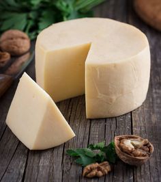 a piece of cheese sitting on top of a wooden table next to nuts and leaves