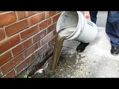 a man is pouring water into a bucket on the sidewalk next to a brick wall