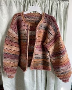 a crocheted cardigan hanging on a curtain rod in front of a window