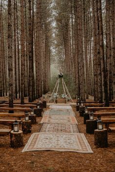 an outdoor ceremony setup in the woods with wooden benches and rugs on the ground