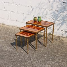 two tables sitting next to each other on top of cement ground in front of a white brick wall