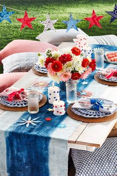 an outdoor table set with plates and flowers on it, along with red white and blue napkins