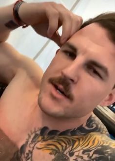 a man with tattoos on his chest is brushing his hair and looking at the camera