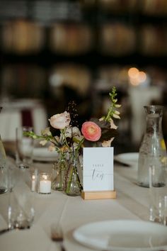 the table is set with white linens and flowers in vases, candles, and menu cards