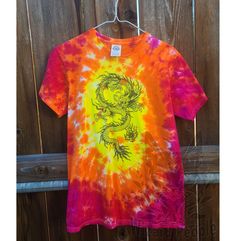 an orange and yellow tie - dye shirt with a dragon on it hanging from a wooden fence