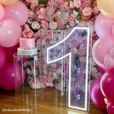 the number one sign is lit up in front of pink flowers and balloon garlands